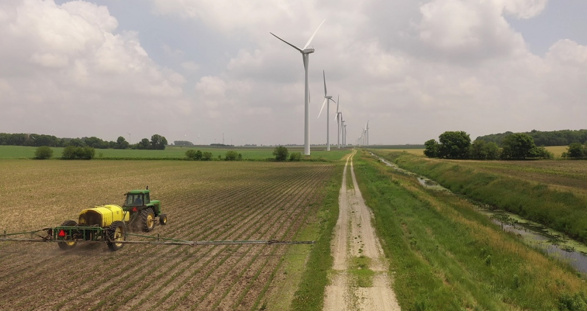 一个农夫在一个字段在草地上湖风电场扩张今年早些时候。2018年康明斯帮助风电场扩大。